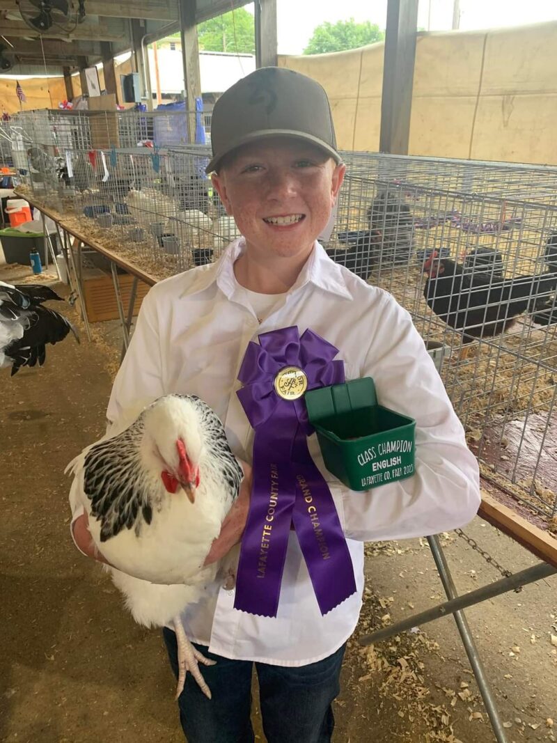 boy wearing purple prize ribbon and holding his prize chicken