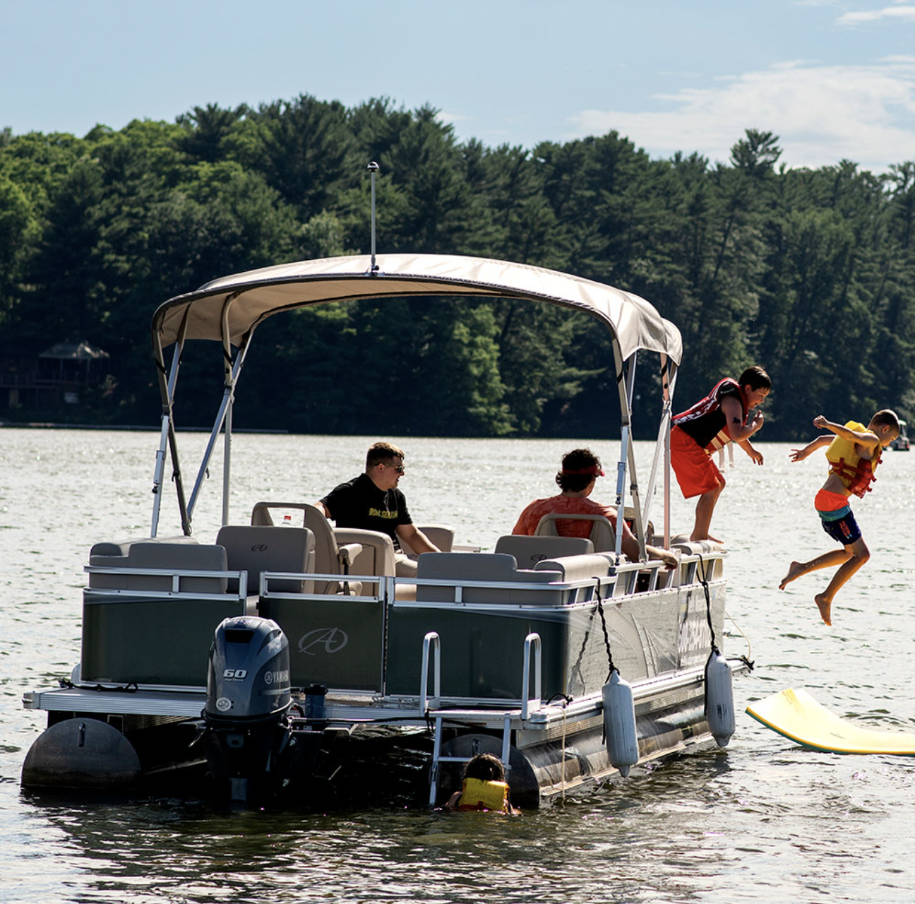 two kids in life jackets jumping off a pontoon boat