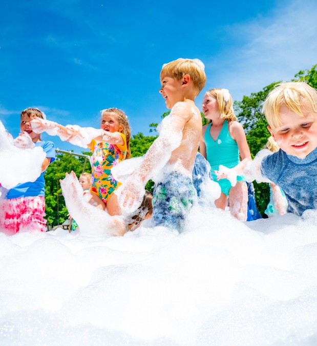 kids in swimsuits playing in foam from a foam machine