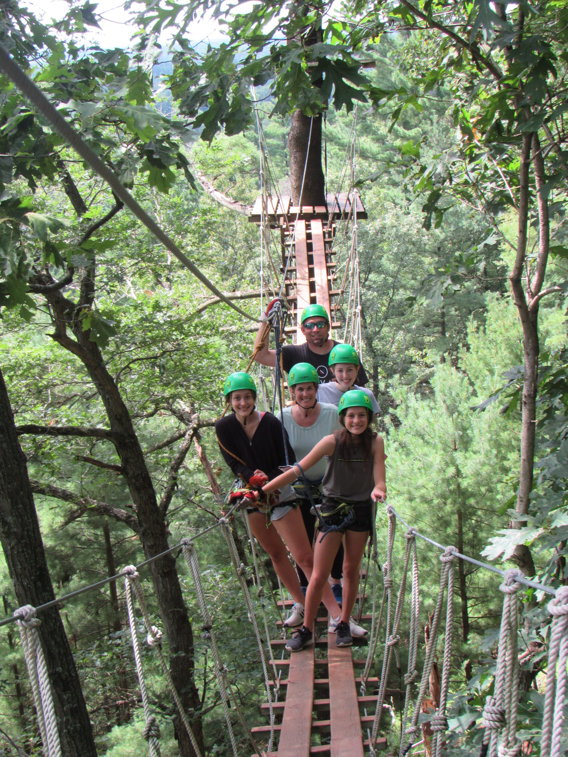 family in helmets standing on a suspended wooden bridge