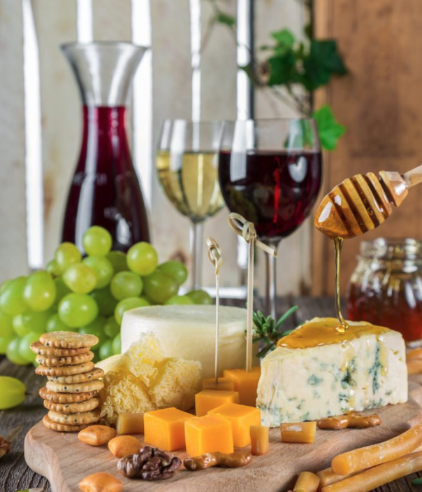 a board of several cheeses in front of glasses of white and red wine