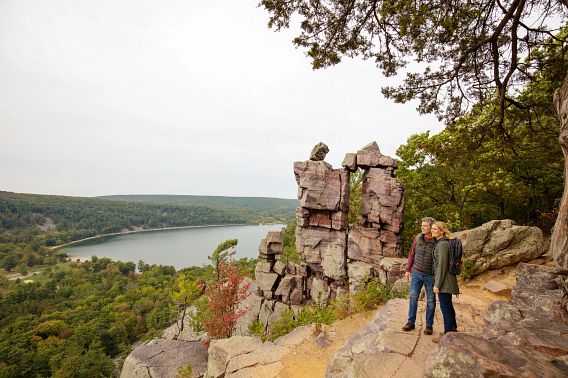 man and woman pose near rock formation at scenic overlook of river and woods