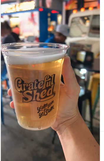 woman's hand holding plastic glass of Grateful Shed beer